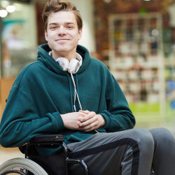 High school student in a wheel chair in the library smiling at the camera.