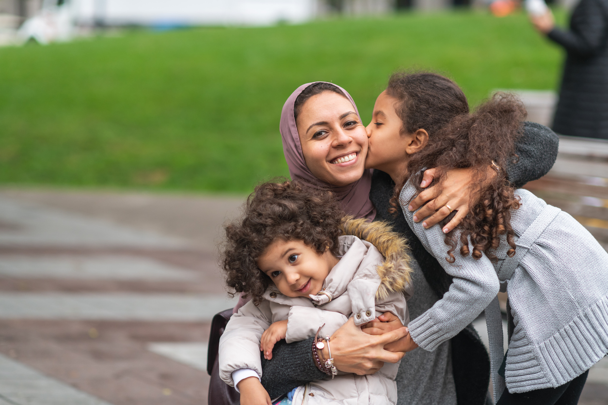 Muslim mother hugging daughters in city park